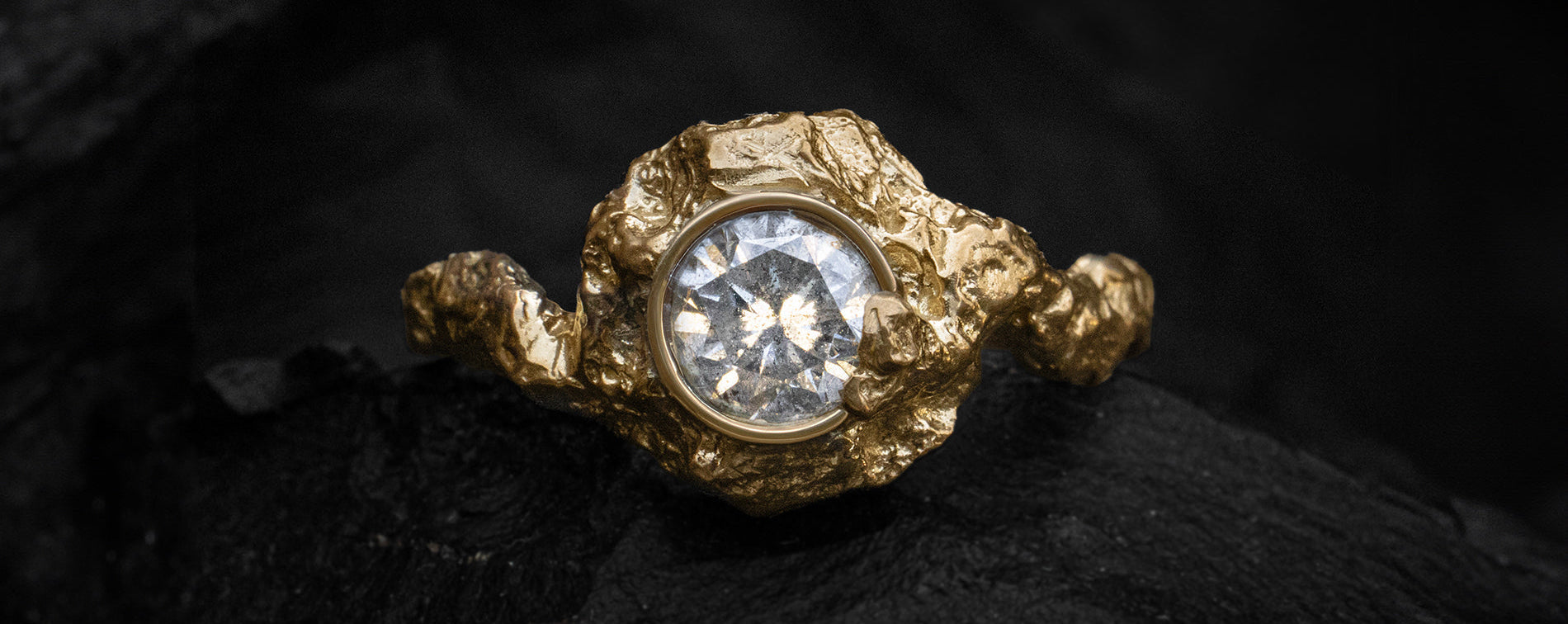 Sculptural gold alternative engagement ring with an icy salt and pepper diamond on a dark background