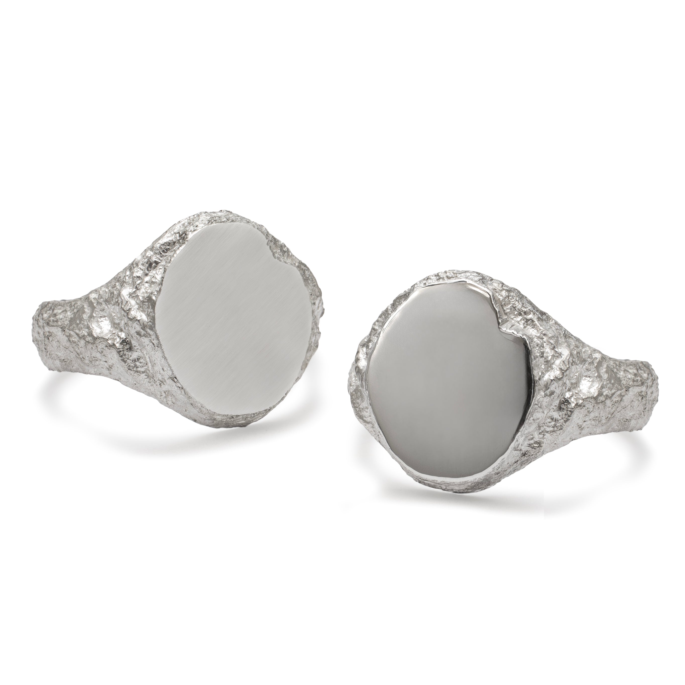Two oval signet rings side by side with textured detail, the left ring has a matte face and the right has a polished face.