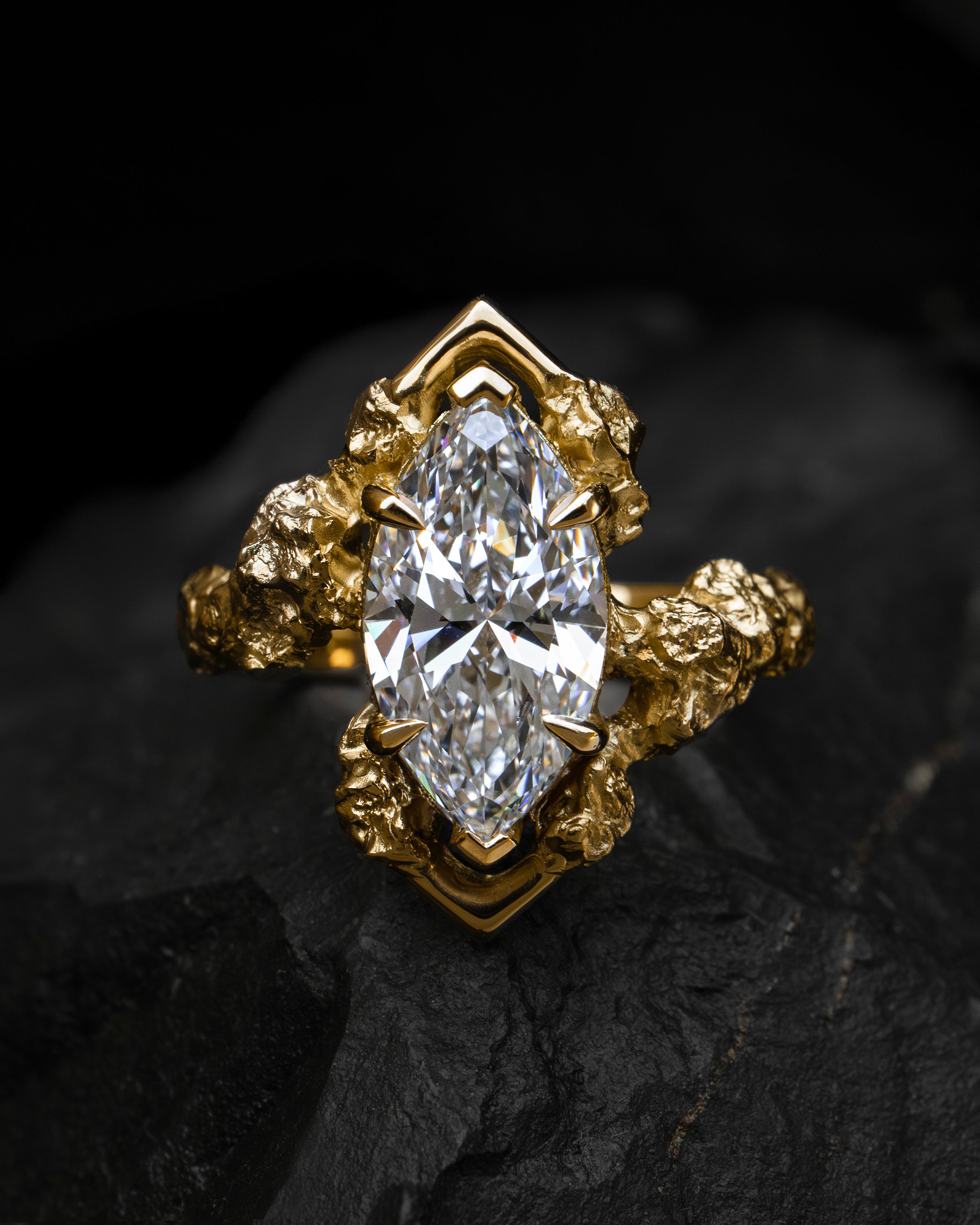 Sculptural yellow gold engagement ring claw set with a pear-shaped diamond on a dark background